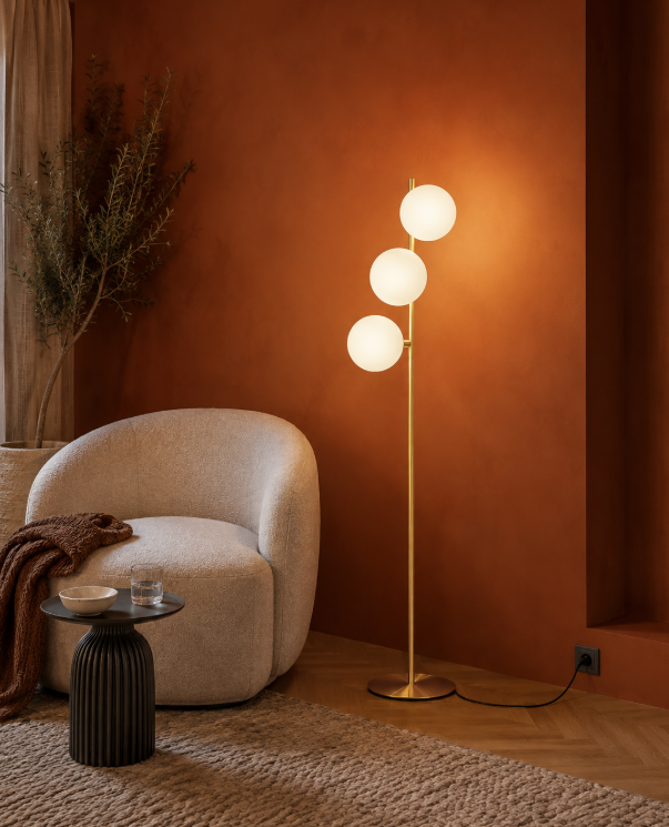 Messing vloerlamp met drie glazen lichtbollen in een warm interieur